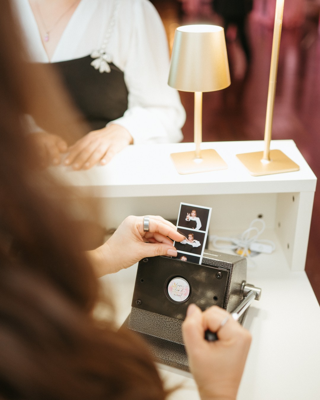 Hands sliding a photo strip into a hand press on a white bar under a gold lamp