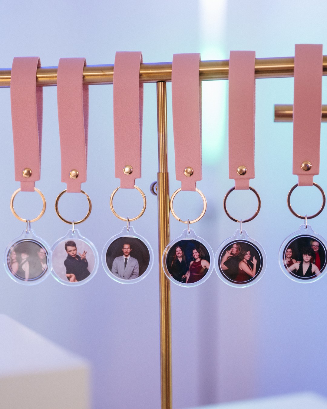 Six finished photo keychains with guests' photos hanging in a row from a gold bar