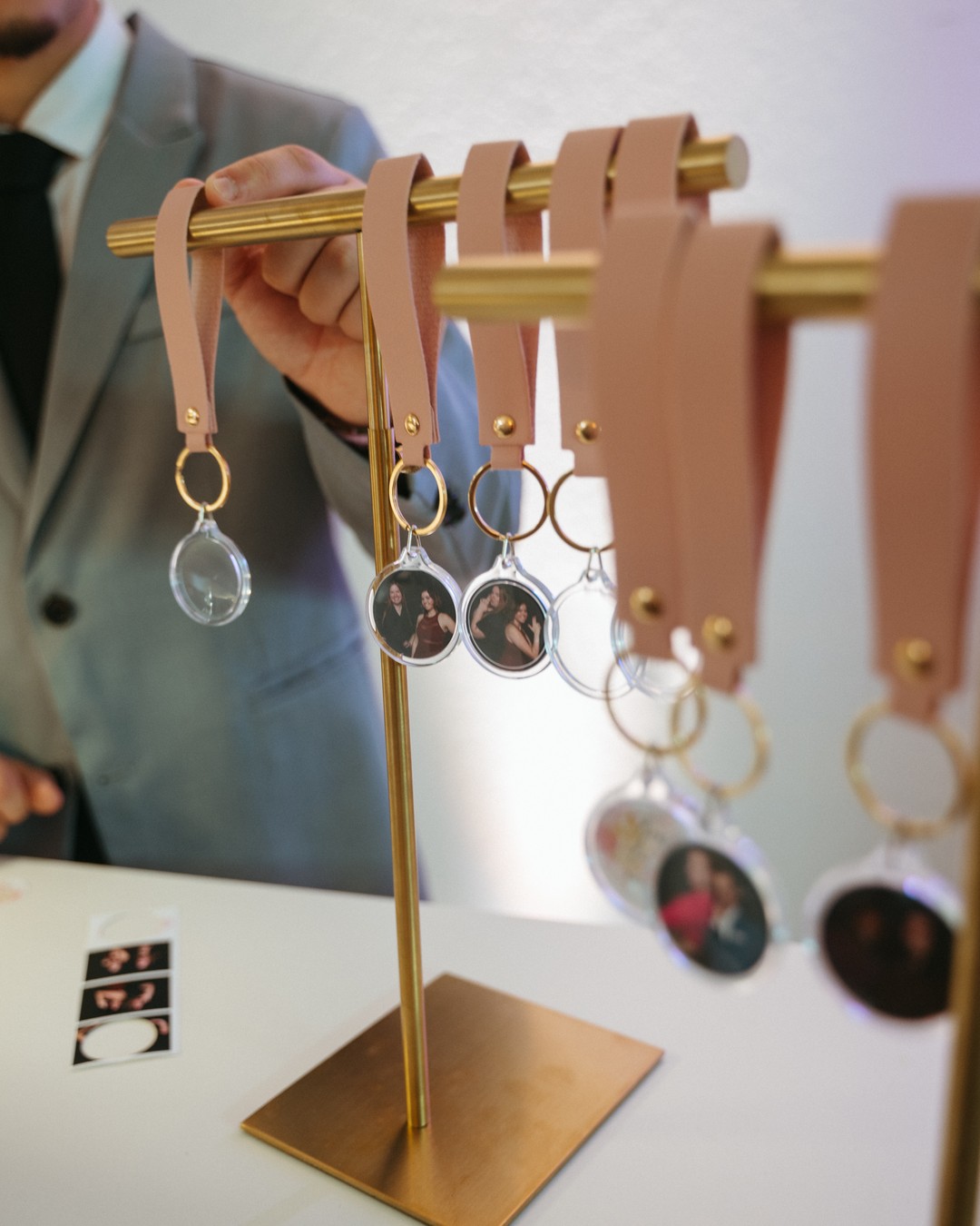 Man in a gray suit reaching for a photo keychain on a gold rack, a photo strip on the bar